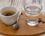 Espresso mit einem Glas Wasser, das die Aromen reinigt. Ein Keks und Kaffeebohnen vervollständigen das Bild.