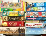 Stos gier planszowych, w tym "Sagrada", "Blokus", "El Dorado", "Everdell", "Catan", "Scythe", "Detektyw", "Carcassonne", "Azul", "Pandemic", "Wsiąść do Pociągu" i "Na Skrzydłach". Idealne gry logiczne dla dorosłych po polsku.