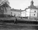En grupp människor samlas framför Rydboholms slott. En kvinna går över gräsmattan.