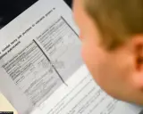 Osoba przygląda się dokumentowi, który pokazuje, jak wygląda mandat z fotoradaru. Widać nagłówek "UWAGA!!" i tekst o podstawie do uiszczenia grzywny.