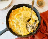 Une tourte aux champignons dorée et appétissante, servie dans une poêle en fonte, avec une cuillère prête à déguster.