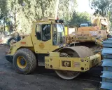 Żółty walec drogowy BOMAG BW 213D-3 na placu budowy, obok koparki Samsung Caterpillar.
