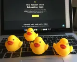 Cztery żółte gumowe kaczuszki siedzą na klawiaturze laptopa, obok ekranu z napisem "The Rubber Duck Debugging tool".