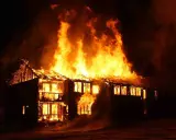 Une maison à deux étages est dévorée par les flammes, le toit s'effondre. L'incendie cause une destruction massive.