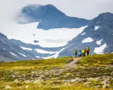 Vandrare med ryggsäckar går längs en stig med glaciärklädda sylarna runt.