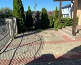 Nowy pomysł na stary chodnik: kostka brukowa w odcieniach beżu i czerwieni tworzy ciekawy wzór przed domem, otoczonym zielenią i ogrodzeniem.