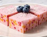 Różowy deser owocowy z kolorowymi kuleczkami i borówkami na talerzu.