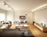 Un salón moderno con sofás grises, mesa de centro blanca y TV. La iluminación, con focos en riel y lámpara de arco, es clave para como iluminar un salón.