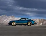 Ein türkisfarbener Porsche 911 SC mit goldenen Felgen und Streifen steht auf einer Bergstraße. Die Wertentwicklung dieses Klassikers ist beeindruckend.