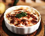 En krämig lasagne vegetarisk med gyllene ost och färska örter, serverad i en vit ugnsform.