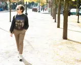 A woman walks down a tree-lined street in a trendy plaid pants outfit, featuring a graphic sweatshirt and white sneakers.