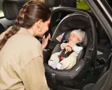 Madre mira a su bebé dormido en la silla coche, asegurando la correcta postura recien nacido silla coche para un viaje seguro.
