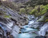 Un río de aguas cristalinas serpentea entre rocas pulidas y vegetación exuberante. Un paisaje idílico que evoca la frescura del verano en Extremadura.