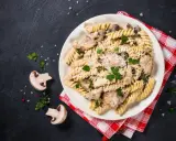 Pyszny makaron z kurczakiem i pieczarkami w kremowym sosie, posypany parmezanem i świeżą pietruszką.