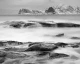 Vatten virvlar runt stenar vid en snötäckt kust. Perfekt för zoom fotoresor.