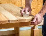 Un artisan utilise un bloc de ponçage pour comment poncer un plan de travail en bois, révélant la beauté naturelle du grain.