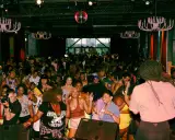 A vibrant crowd dances at a lively event, possibly one of the best gay bars in Chicago, under a disco ball and ornate chandeliers.