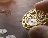 Un orologiaio assembla i componenti di un orologio meccanico, mostrando ingranaggi e molle dorate.