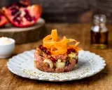 Deliziosa tartare di manzo con melograno, cipolla e carote a spirale, servita su un piatto rustico.