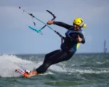 Uśmiechnięty mężczyzna w żółtym kasku i piance cieszy się jazdą na desce. To świetna nauka kitesurfingu!