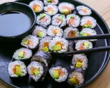 Un plato negro lleno de maki sushi de salmón y aguacate, listo para ser disfrutado con salsa de soja.