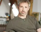 Gavin Wood, z siwiejącymi włosami i kilkudniowym zarostem, w zniszczonej zielonej koszulce, siedzi w przytulnym wnętrzu.
