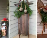Idées de décoration Noël extérieur à faire soi-même : skis anciens, traîneau vintage, raquettes ornées de verdure et de cloches.