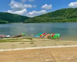 Jezioro Klimkowskie plaża z kolorowymi rowerami wodnymi i kajakami, otoczona zielonymi wzgórzami.