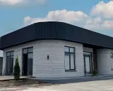 Ein modernes 3d druck haus mit runden Ecken und einem dunklen Dach steht unter einem blauen Himmel mit Wolken.