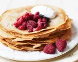 En hög med glutenfria pannkakor toppas med färska hallon och en klick grädde. Perfekt för en frukost eller fika.