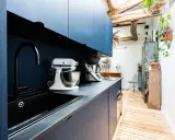 Cuisine moderne avec armoires bleues, évier noir et robot pâtissier. L'entrée de la maison donne directement dans cette pièce fonctionnelle et stylée.