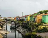 Cabanes colorées alignées le long d'un canal, un bateau amarré. Un charmant port sur l'Île d'Oléron.
