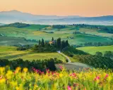 Un casale solitario su una collina, circondato da cipressi e dolci colline verdi, un sogno per un tour della Toscana.