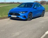 Blauer Mercedes-Benz CLA 250+ EQ auf einer Straße, mit grünen Feldern und einem Strommast im Hintergrund.