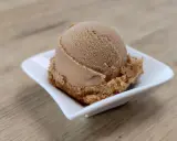 Eine Kugel cremiges Coca Cola Eis in einer weißen Schale auf Holzhintergrund.