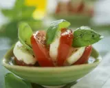 Tomate Mozzarella, ein gesundes Gericht, garniert mit frischem Basilikum und Pfeffer, serviert in einer grünen Schale.