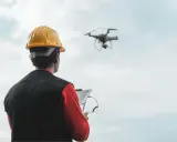 Operator drona w żółtym kasku steruje maszyną za pomocą tabletu.