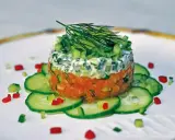 Wykwintny tatar z łososia, ułożony warstwowo z kremowym sosem i świeżymi warzywami, ozdobiony koperkiem.