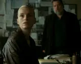 Kobieta w skórzanej kurtce i mężczyzna z brodą w tle, atmosfera napięcia w stylu thriller skandynawski film.