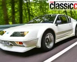 Weißer Renault Alpine A310 fährt auf einer Straße durch einen grünen Wald.