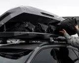 Mężczyzna wkłada torbę do największego boxu dachowego Thule, przygotowując się na wyprawę.