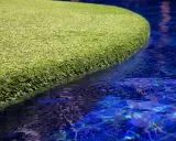 A vibrant green artificial grass island floats in a bright blue pool. The question of will chlorine kill grass is answered by this synthetic turf, unaffected by the water.