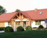 Urokliwy dom w stylu kolonialnym z czerwoną dachówką, ceglanymi detalami i drewnianą werandą, otoczony zielenią.