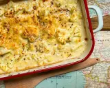 Coliflor gratinado con bechamel cremosa, cubierto de queso dorado y pimienta negra, servido en una fuente roja sobre un mapa antiguo.