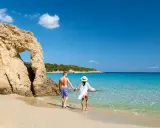 Para, trzymając się za ręce, spaceruje po piaszczystej plaży z turkusową wodą. Czy Cypr jest bezpieczny? Tak, to idealne miejsce na wakacje.