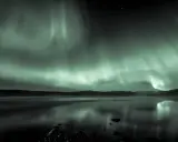Ett magiskt vitt norrsken dansar över en spegelblank sjö i norra Sverige. Stjärnor glittrar i den mörka himlen.