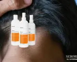 Trzy białe butelki z pomarańczowymi etykietami: szampon, emulsja i lotion SEBORH. Pomagają w walce z łzs.