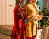 Dwie kobiety w stylizacjach w stylu retro, jedna w czerwonej sukience, druga w żółtym kostiumie, trzymająca kulę z rybkami.