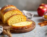 Un pain au pomme doré, tranché sur une planche en bois, avec des pommes rouges et des feuilles d'automne en arrière-plan.