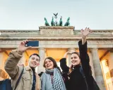 Tre glada vänner tar en selfie framför Brandenburger Tor, en ikonisk sevärdhet att se i Berlin.
